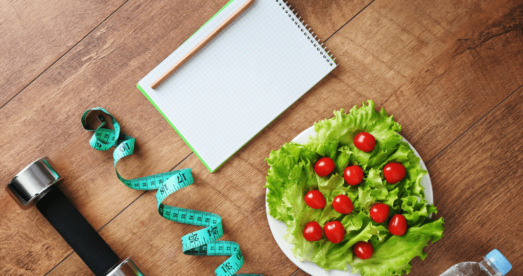 Fitness items and healthy salad on a wooden surface