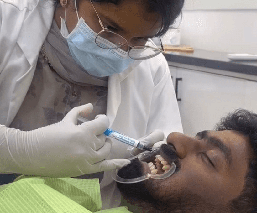 Dental professional performing procedure on patient using instruments and suction in clinic setting.