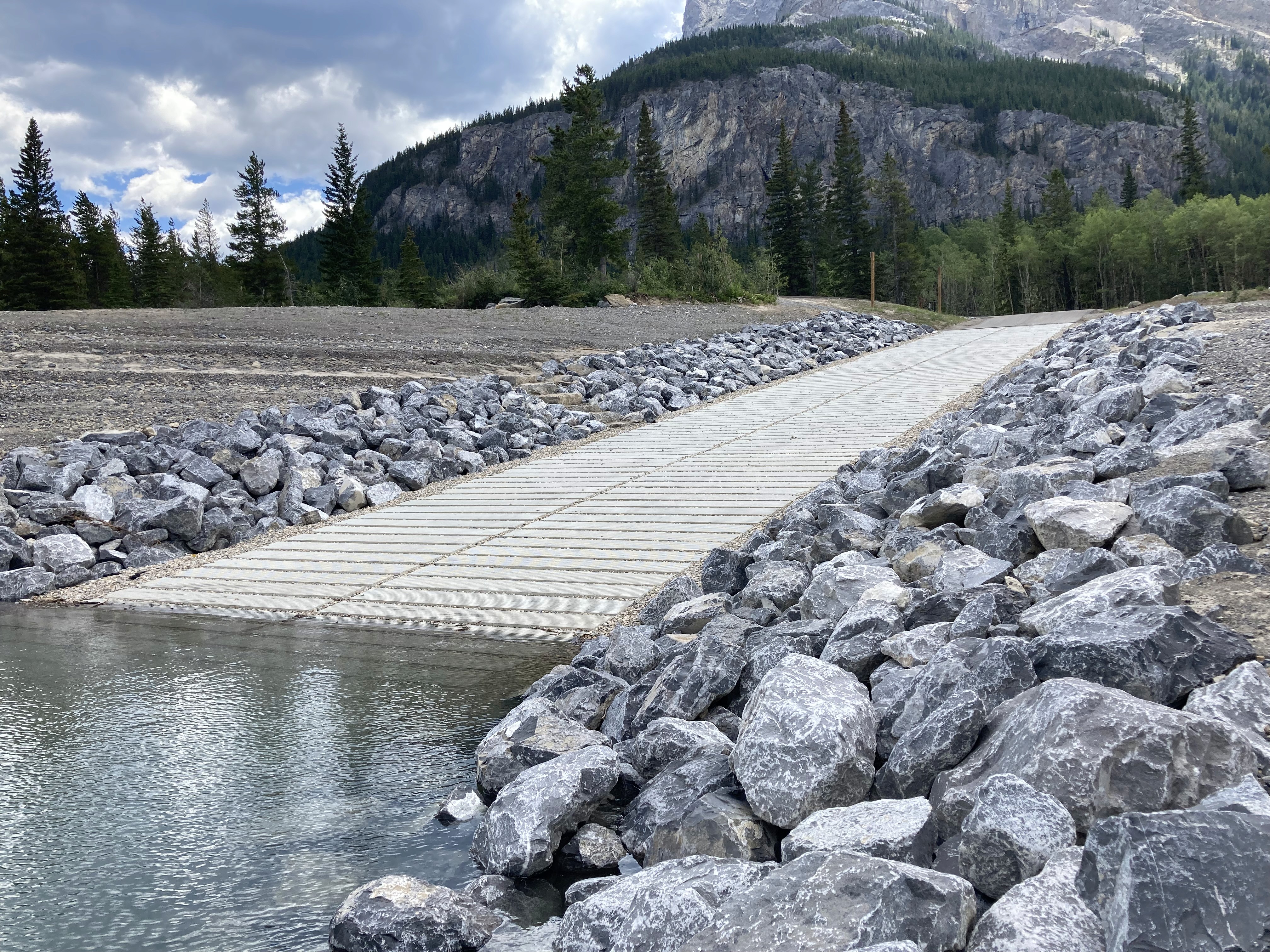 Boat launch access ramp with riprap bank armoring and mountain landscape at Barrier Lake
