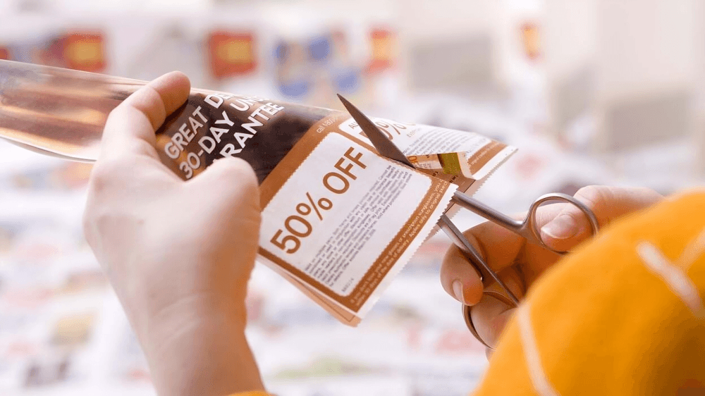 Person cutting out a 50% off paper coupon