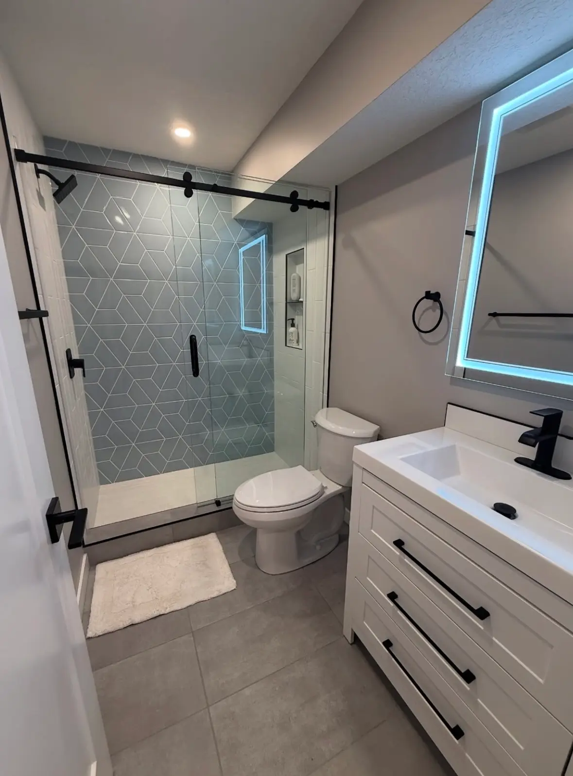 Clean bathroom featuring a streak-free glass shower door, polished black fixtures, and a sanitized white vanity with a glowing LED mirror.
