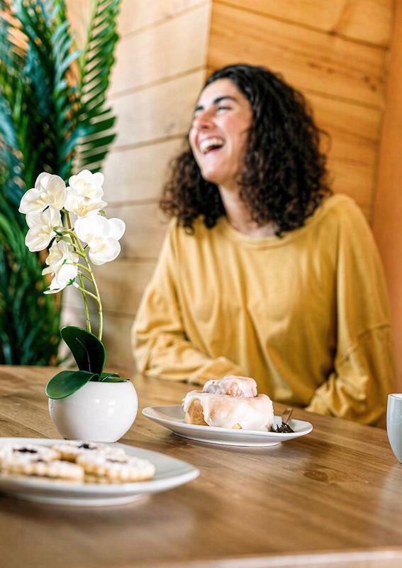 Cinnamon rolls and assorted cookies on a table in a cozy café, with a blurred woman sitting in the background.tcha cookie split open showing its chewy interior.