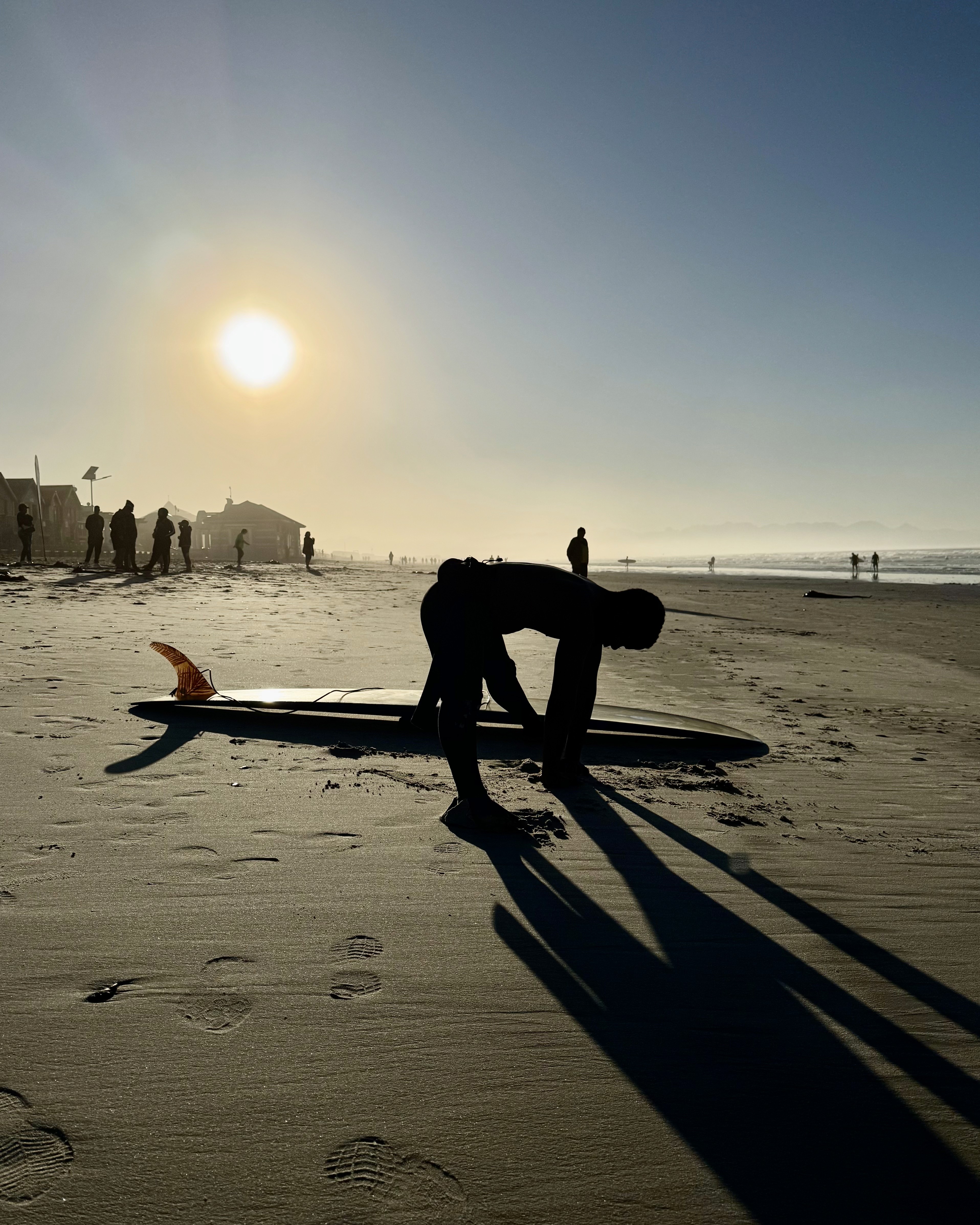 A male surfer stretching at the beach next to his surfboard, about to head into the water at Muizenberg beach in Cape Town