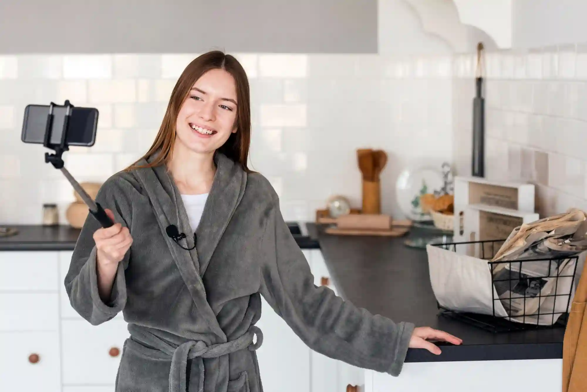 Woman in a bathrobe filming a casual 'morning routine' or 'day in the life' video in her kitchen.