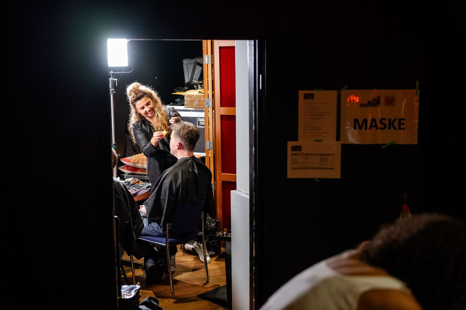 Makeup artist applying cosmetics in a backstage setting with bright lighting.