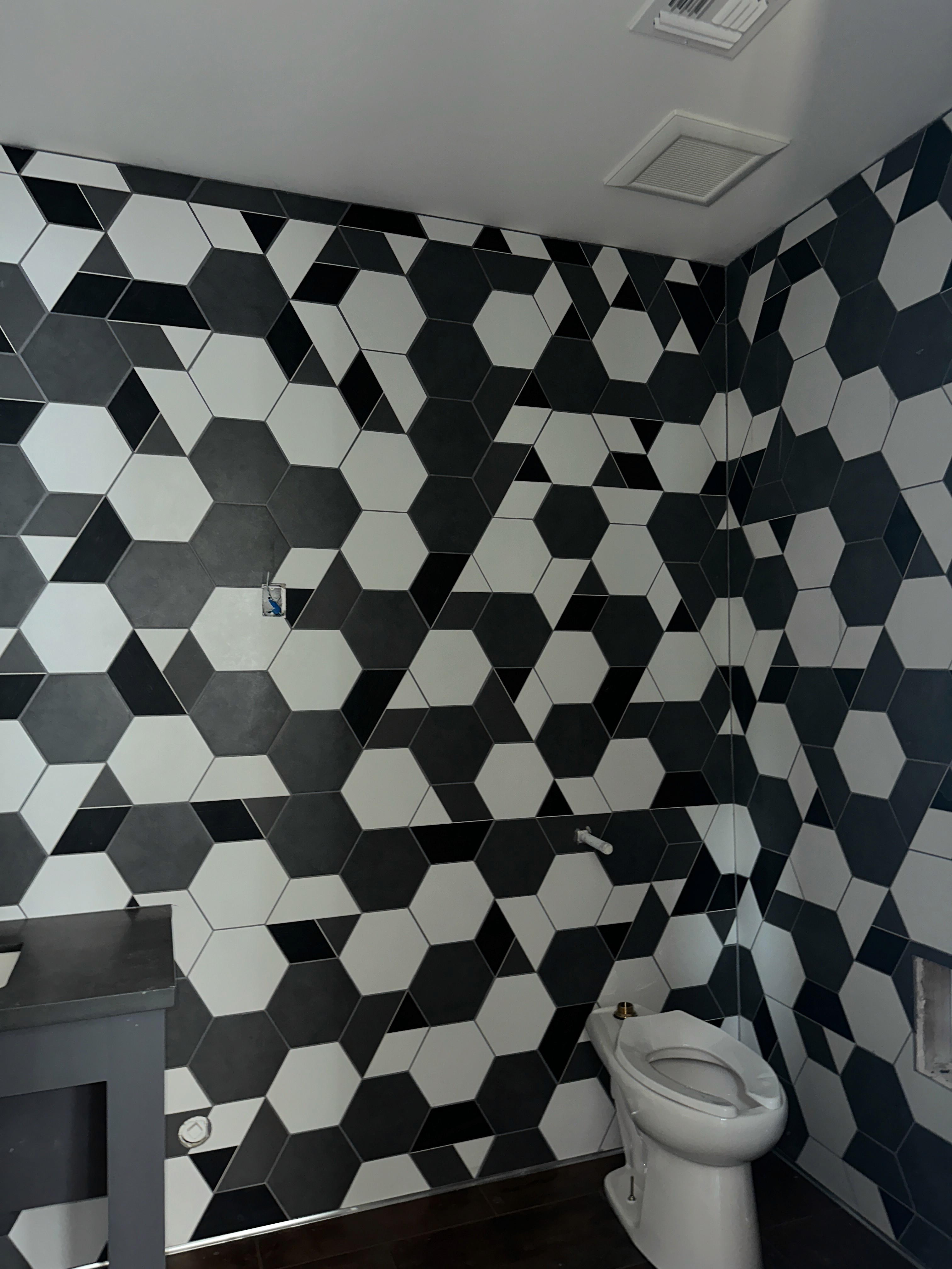 Stylish bathroom featuring a black and white hexagonal tile pattern covering the walls and a toilet.