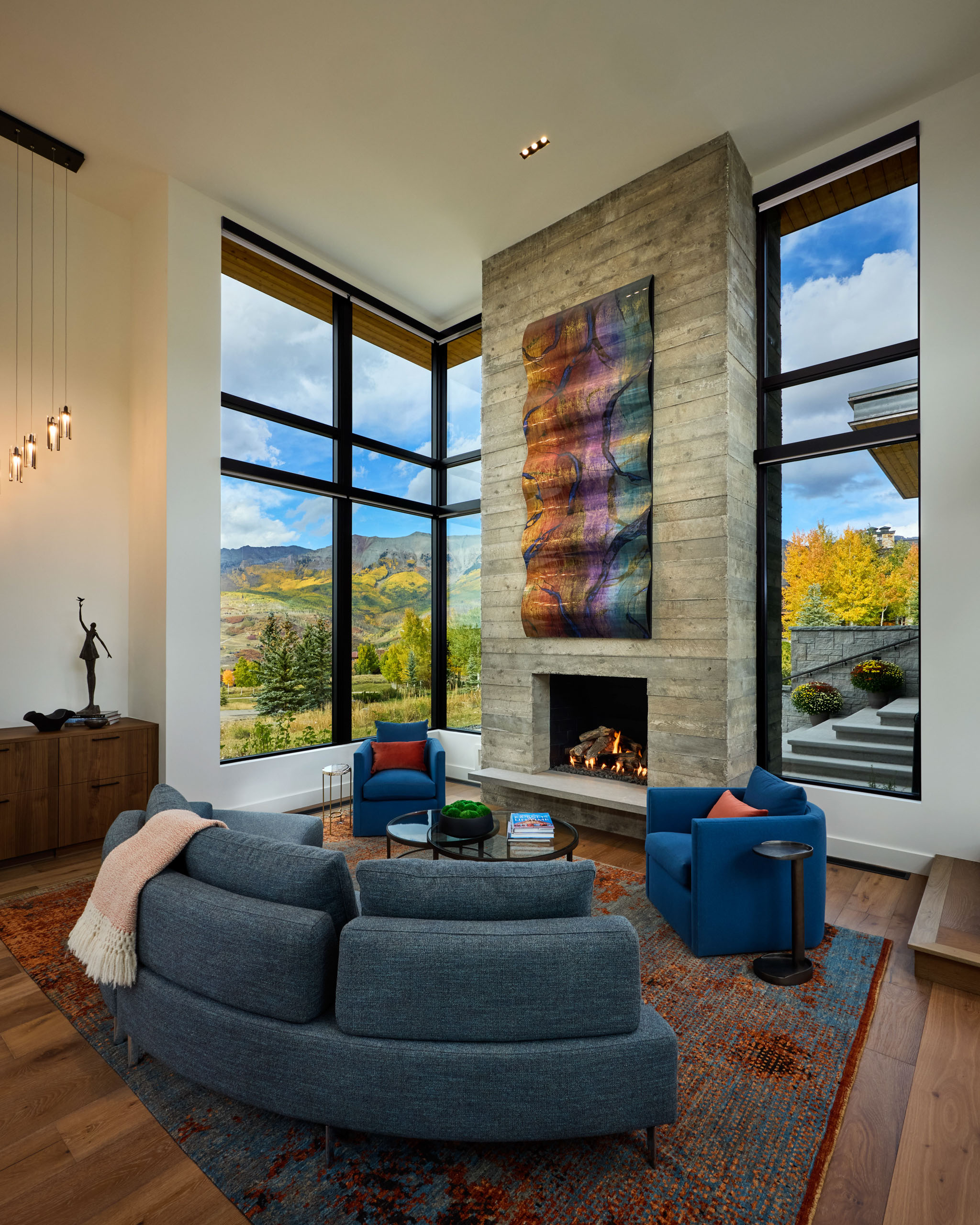 Curved blue sofa, fireplace, and large windows with mountain views.