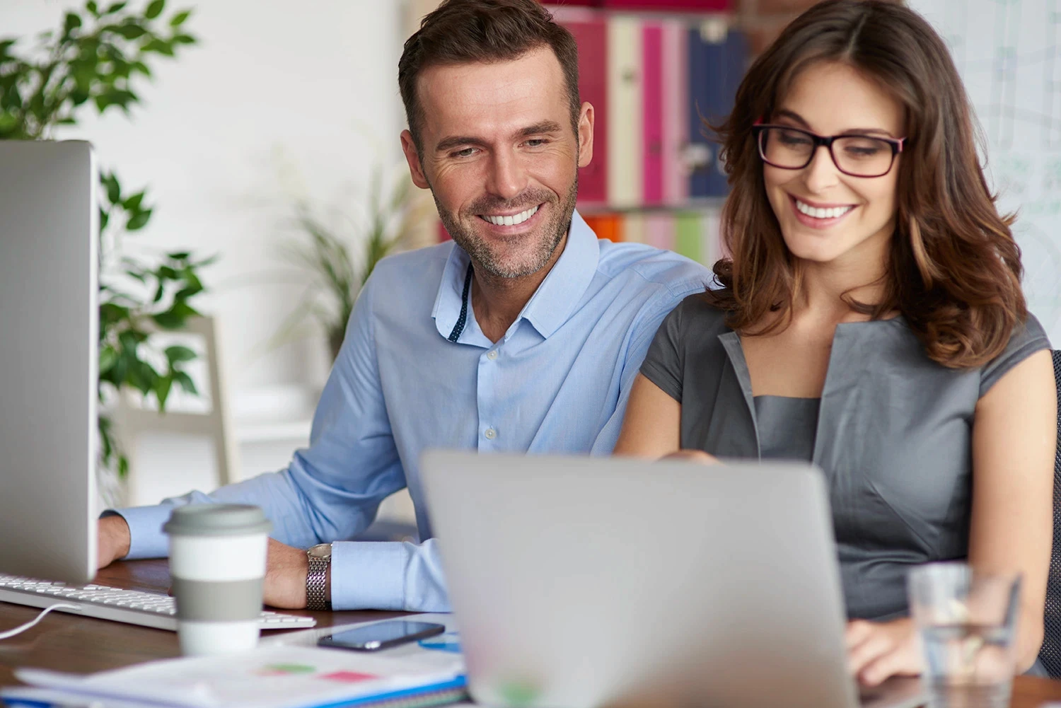 Man and woman smiling broadly while looking at a computer screen together.