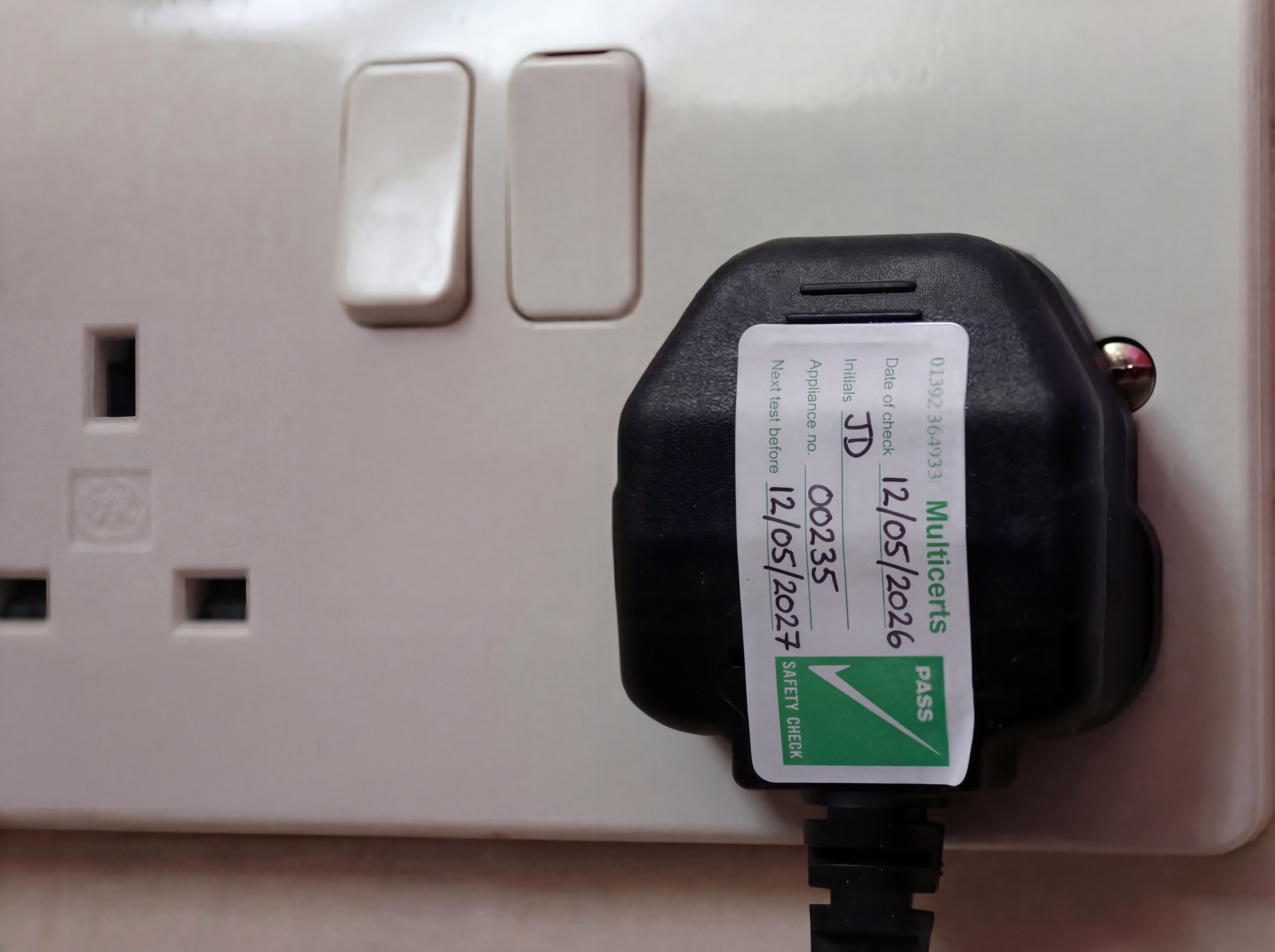 Plug with PAT test label in a wall socket