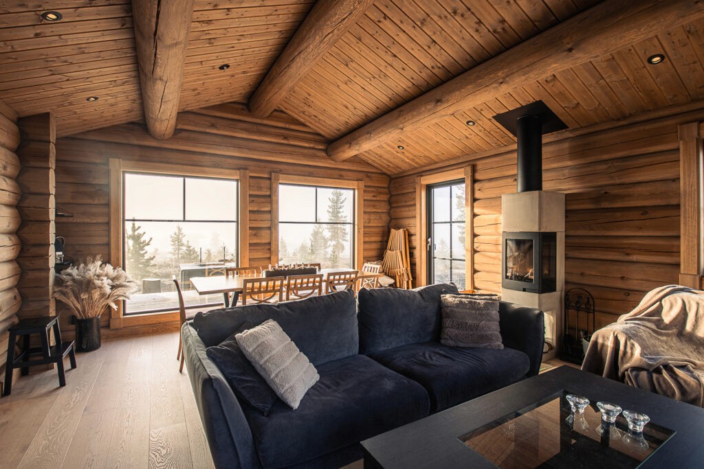 Rustic living room interior with dining table and compact fireplace in a 72 sqm log cabin.
