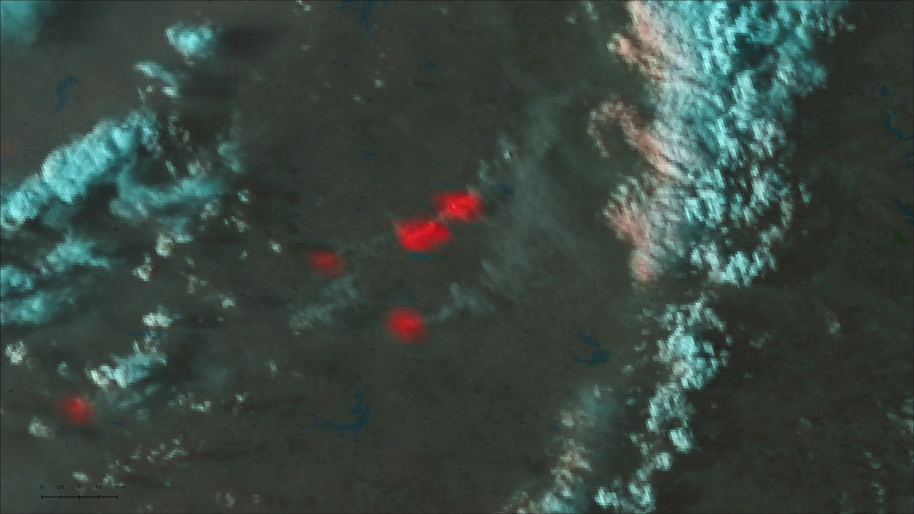 Satellite image displaying a dark landscape with bright red patches indicating areas of volcanic activity or thermal hotspots against a backdrop of blue and gray hues.