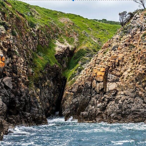 Скалисти крайбрежни скали с тясна, зелена, покрита с мъх долина между тях, водеща към океана с бурни вълни.