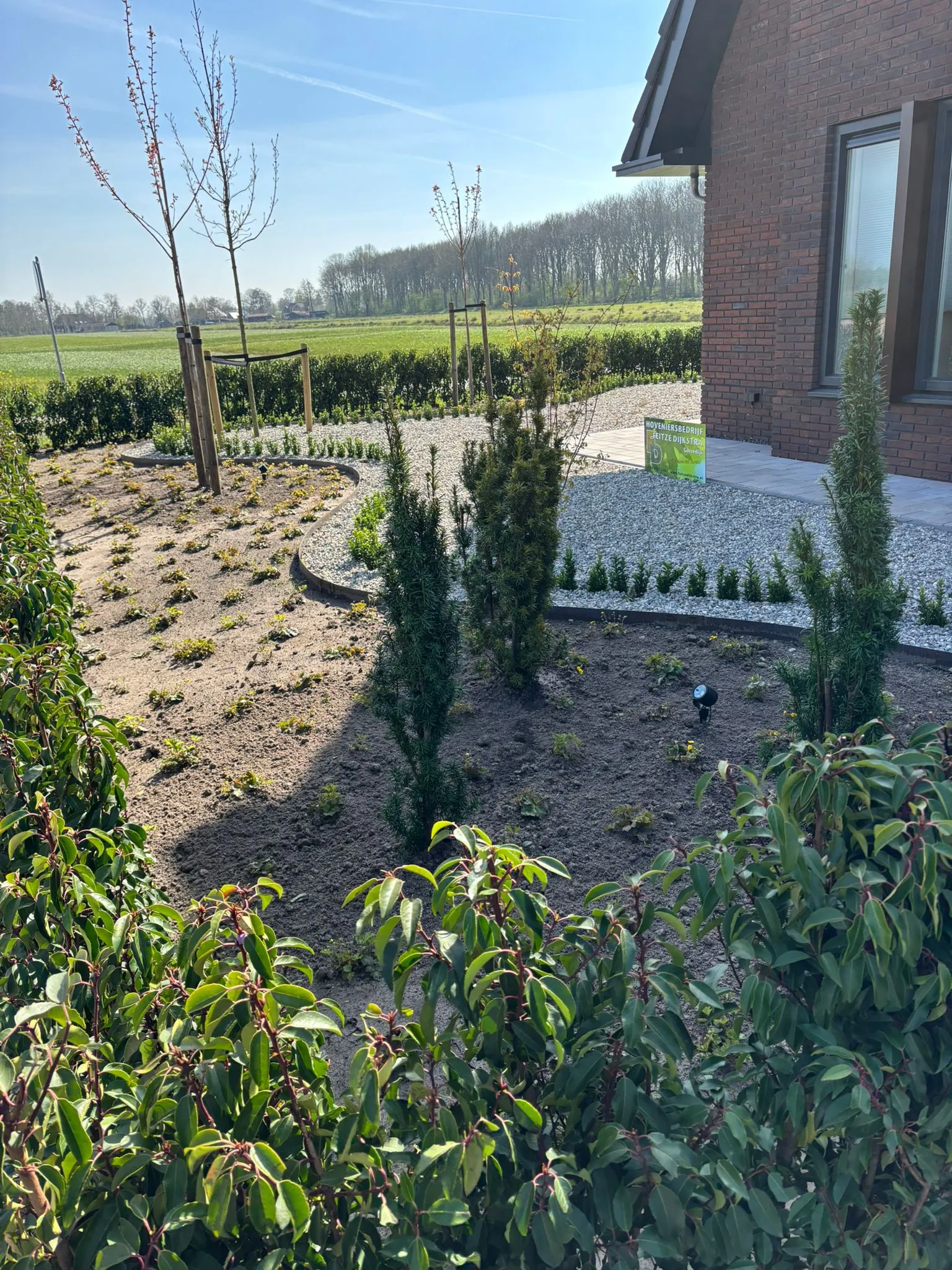Rustige Japanse tuin met jonge bomen, struiken en grindpad naast een bakstenen nieuwbouwwoning in Gorredijk, Friesland.