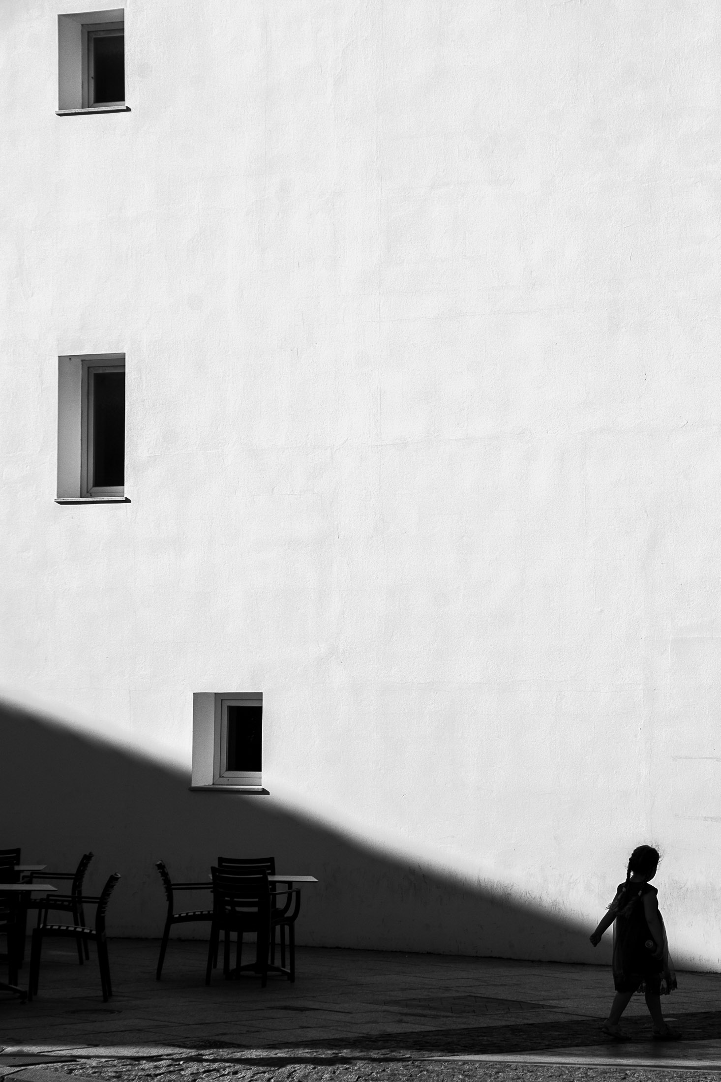 Minimal white building facade with three small windows and a child walking in shadow.