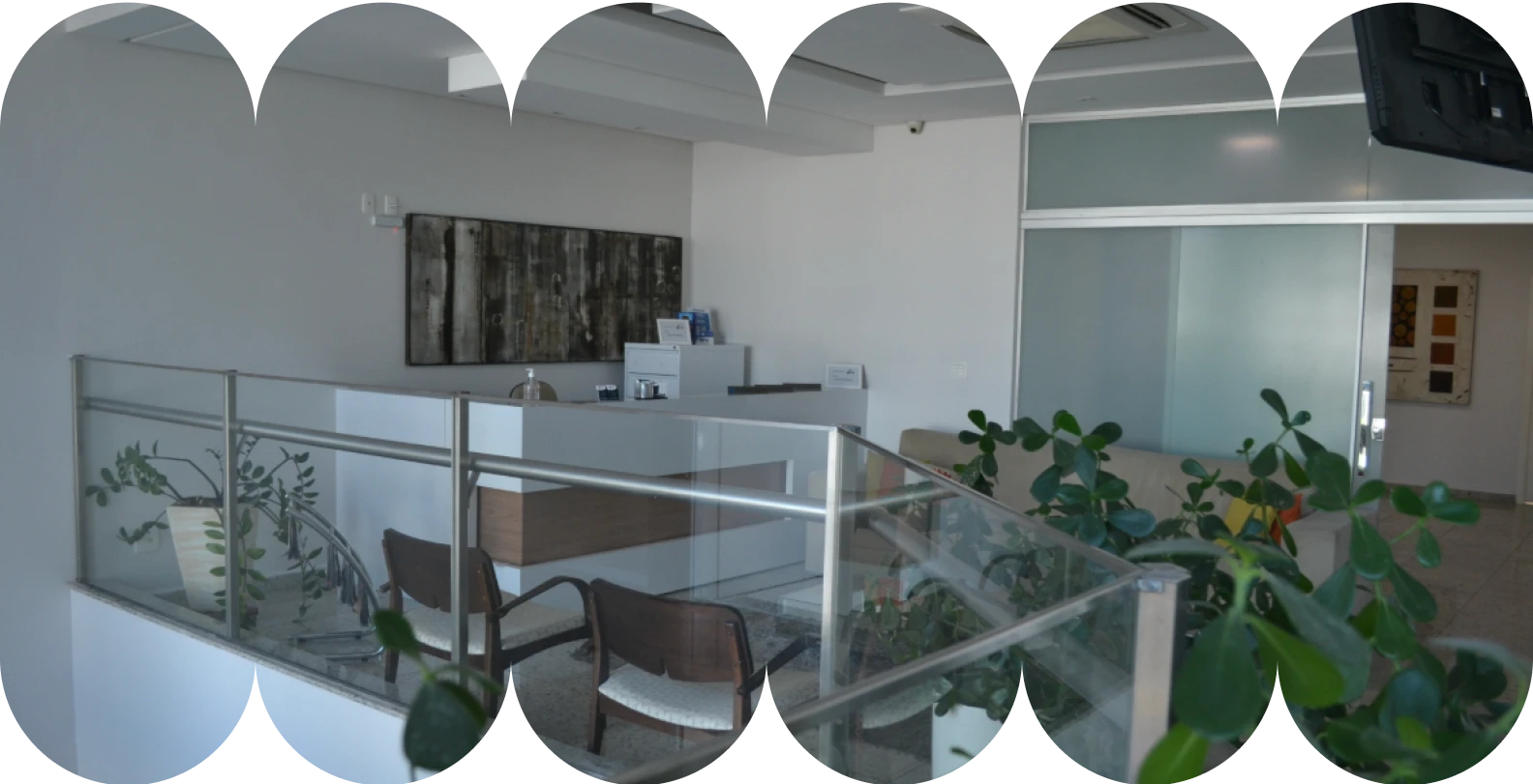 Imagem da recepção e sala de espera de uma clínica ou Hospital-Dia, com balcão branco, móveis modernos, uma escada com guarda-corpo de vidro e plantas decorativas.
