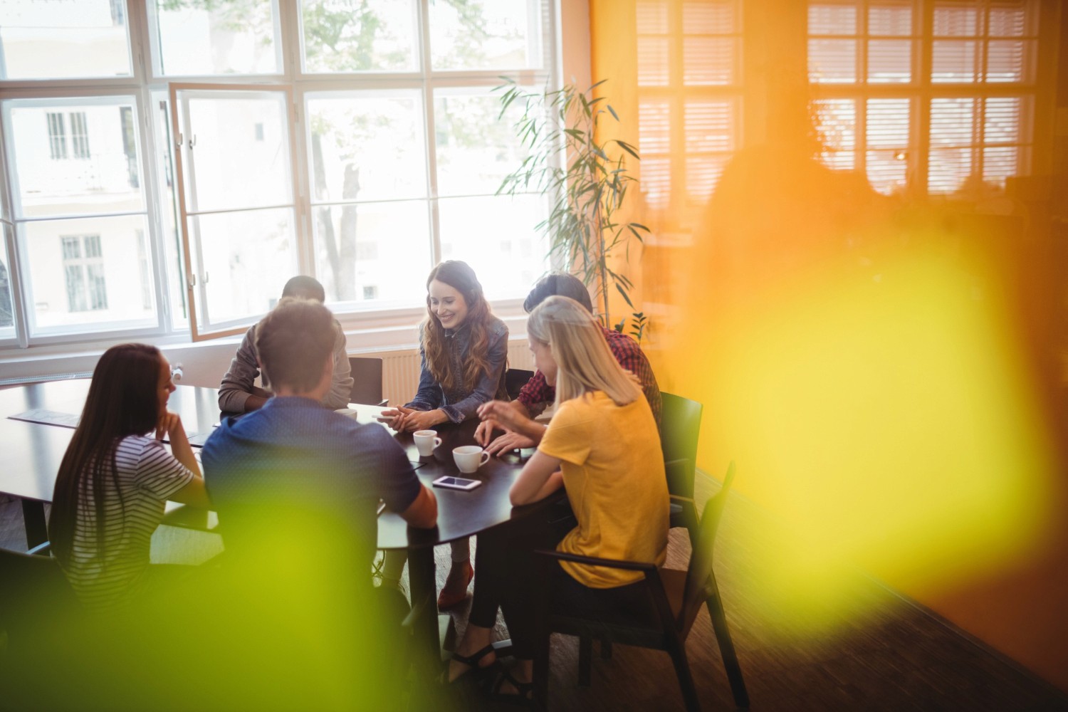 Image of people in a well lit room sat at a large table.