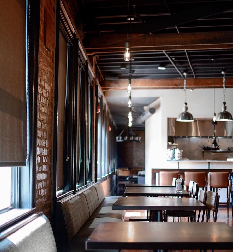 A modern event space with tables set for dining, lush greenery in the center, and bright lighting above.