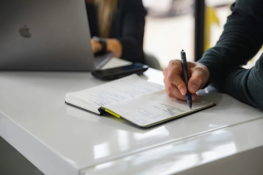 Close-up of a person's hand writing notes in a notebook at a desk.