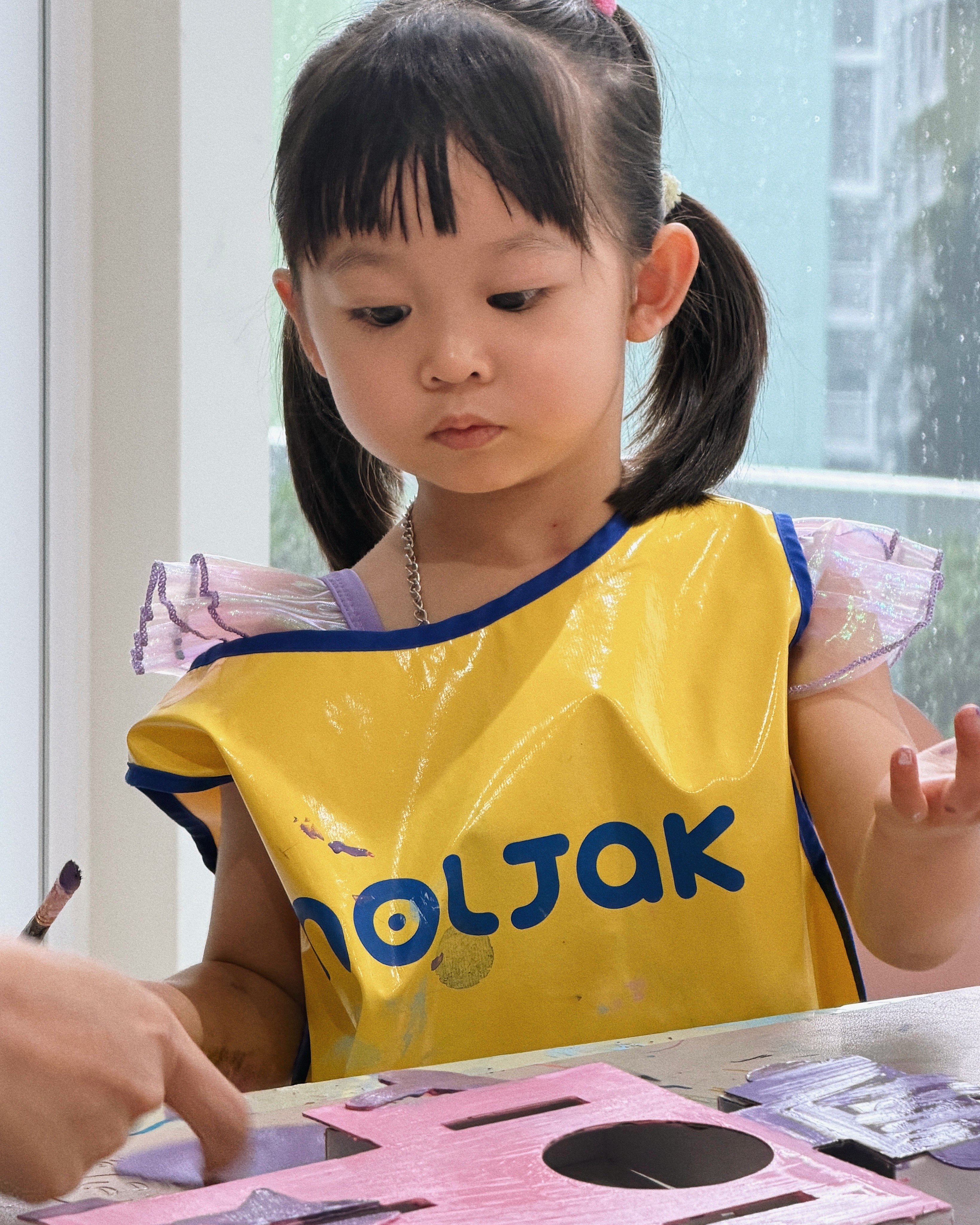A young girl intently observing a three-dimensional cardboard robot structure during a Kiddler design and painting class at Rookids BGC.