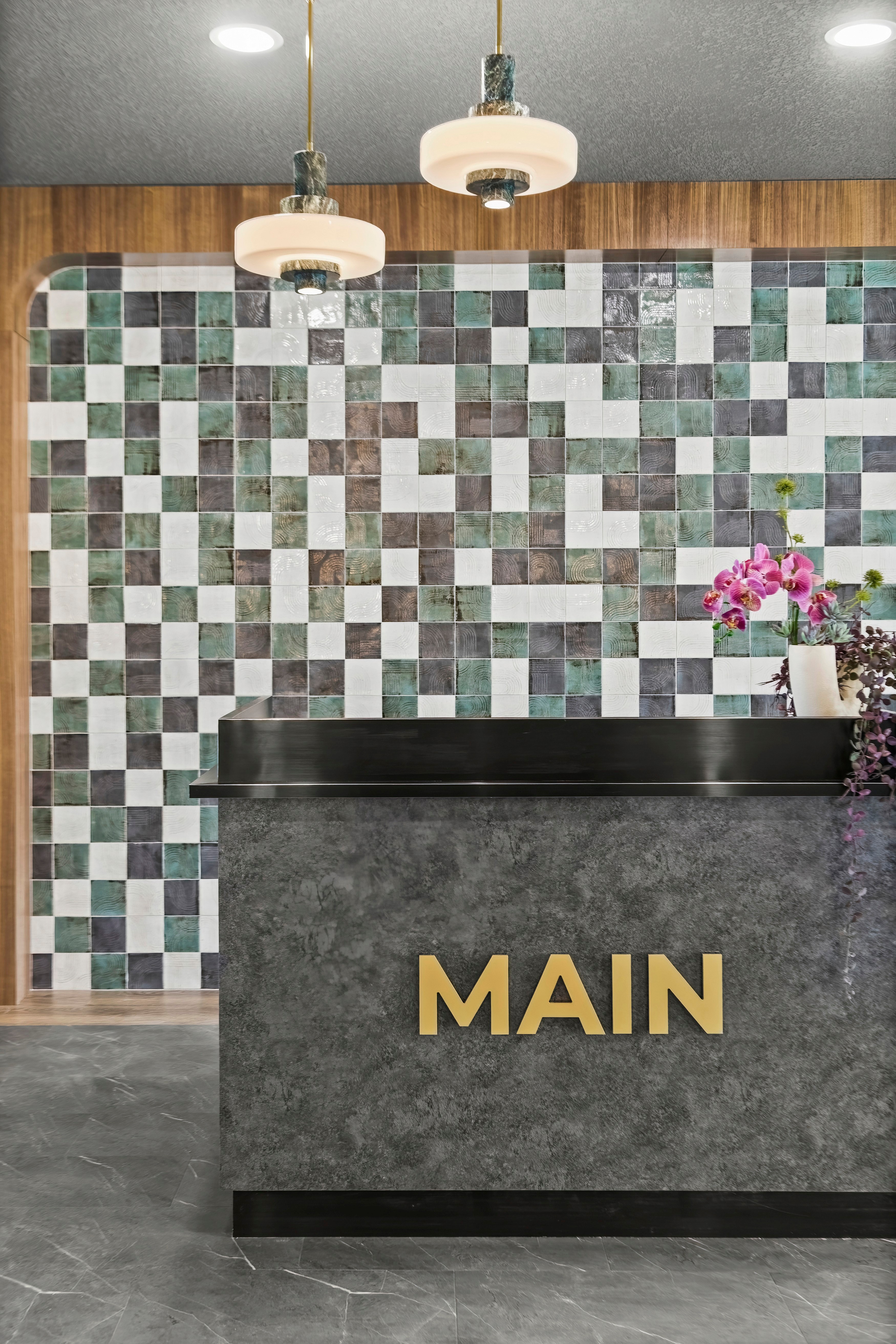 Dean's Landing grey stone reception desk against a sage and forest-green ceramic tile portal, designed by HAUS Interiors, Calgary