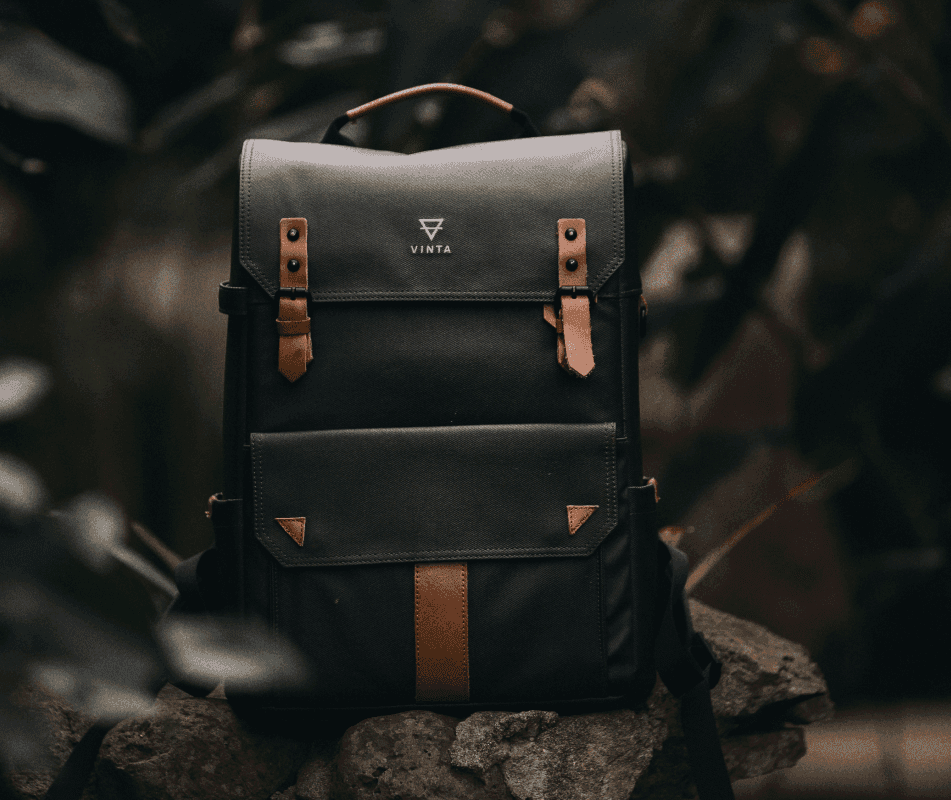 Black FeLuxe backpack with tan leather straps resting on a rock