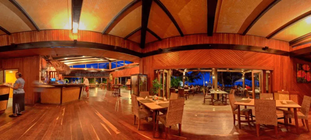 Uprising Beach Resort's spacious dining and bar area, with timber walls and floors, open to the Fiji night sky.