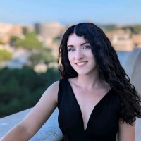 Portrait of a woman with blonde hair in a bun, light denim shirt, smiling.