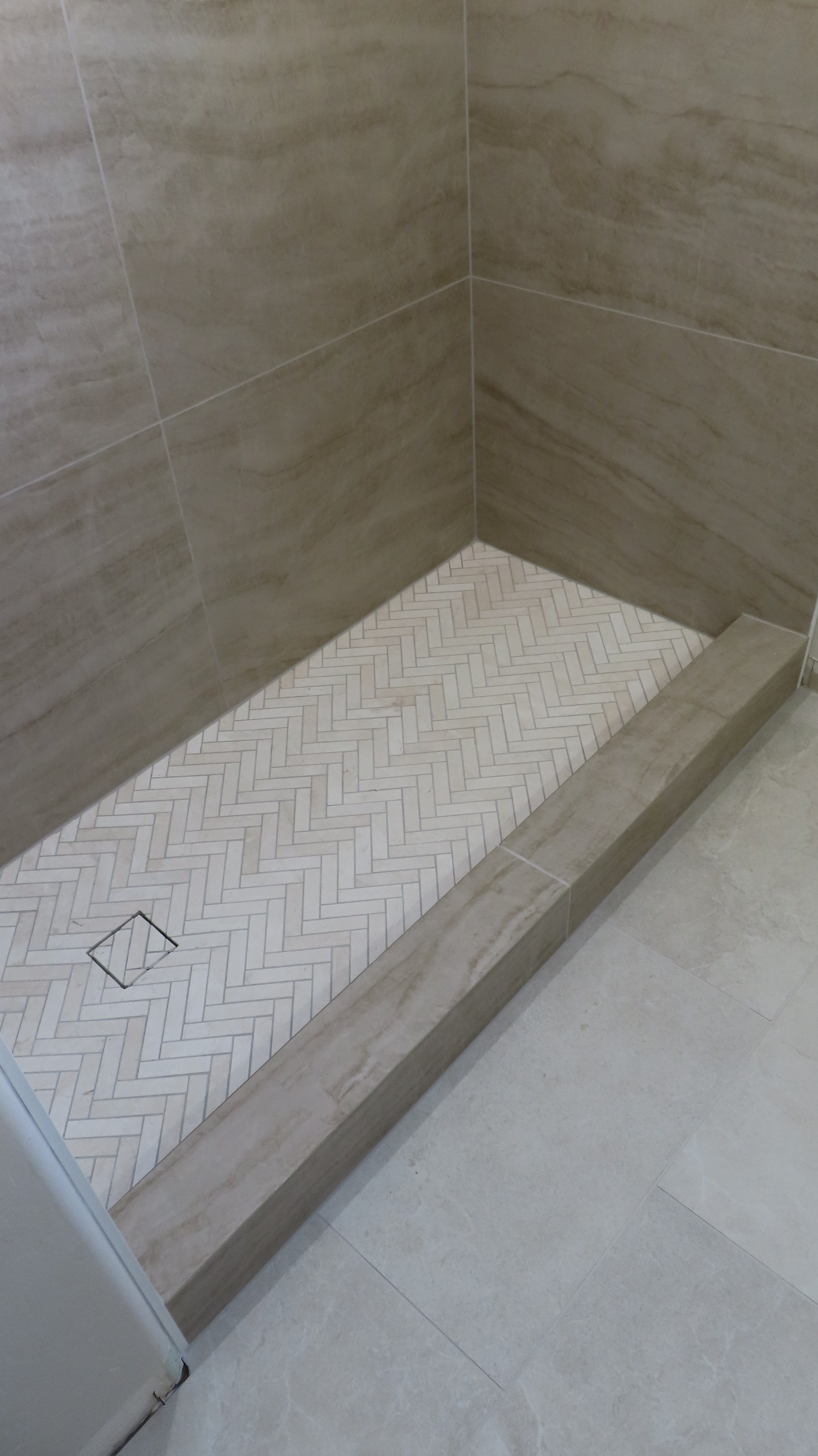 Custom shower wall with large format white marble-look tiles and three built-in rectangular shower niches with contrasting black trim.