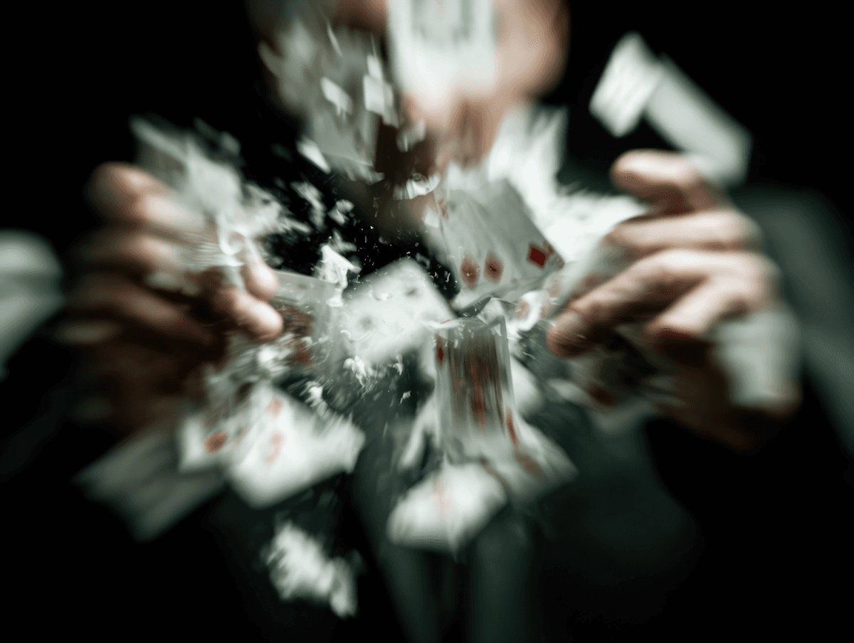 A dramatic scene of playing cards scattering in motion, with hands dispersing them against a dark background, creating a sense of action.