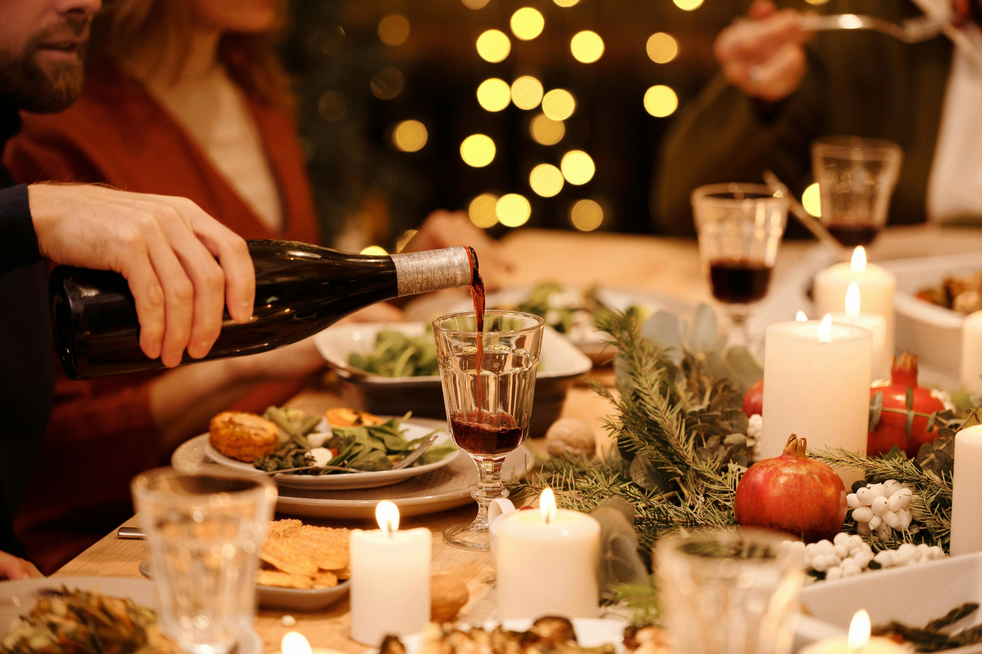 Ein gedeckter Weihnachtstisch, an dem jemand ein Glas Wein einschenkt