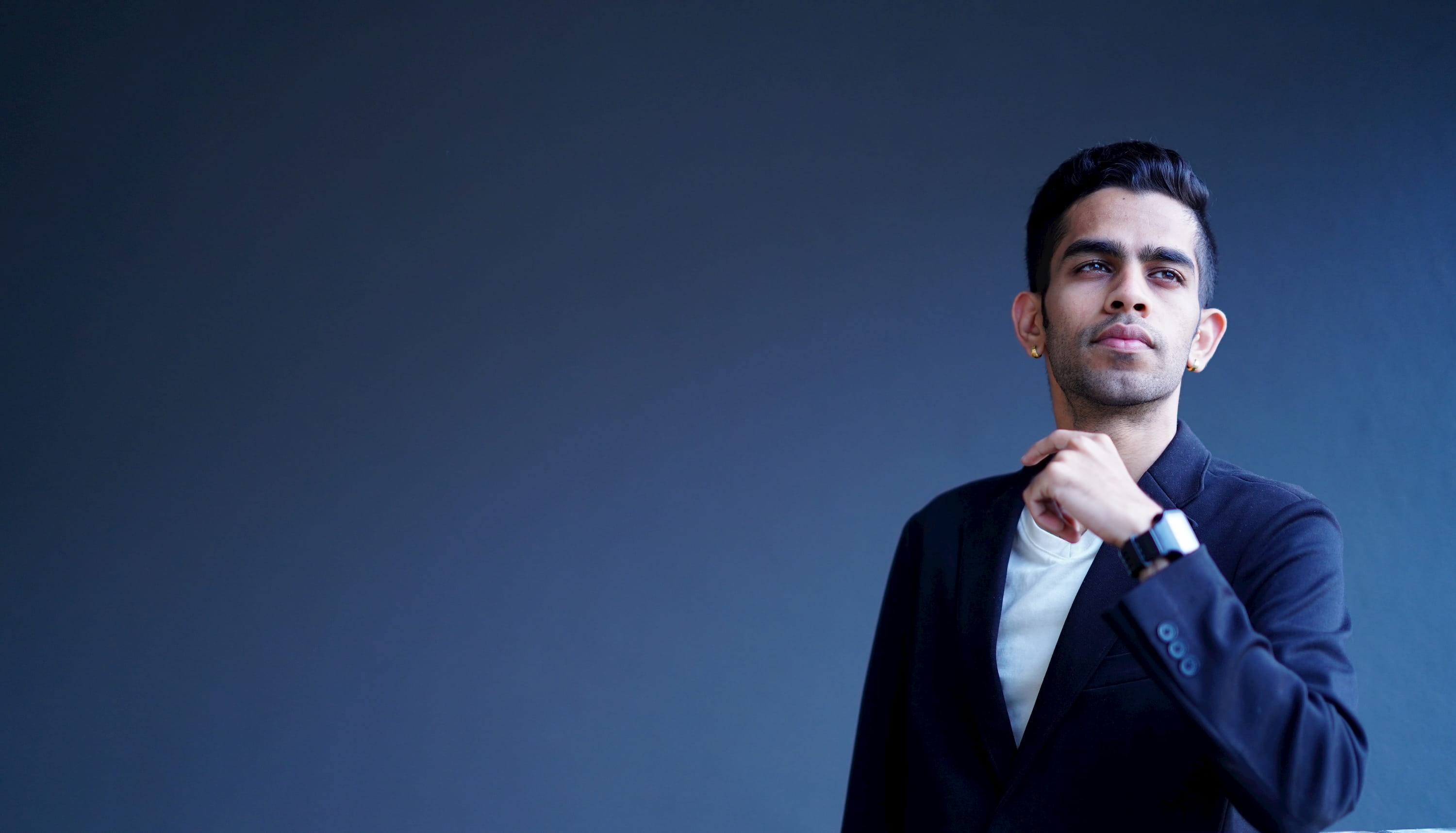 This encapsulates the founder of fyndflow, a young well-groomed professional flaunting a black blazer over a crisp white shirt. Strands of dark hair and a smart beard further amplify his appeal while his subtle smile painted against the vibrant blue backdrop divulges an air of calmness around him. This endearing persona may indeed resonate with that of a life coach in Bangalore, adept at guiding individuals through tumultuous paths with composed serenity where people can discover holistic life coaching solutions powered by FyndFlow.