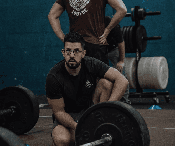 A man squatting behind a loaded barbell in a gym, preparing to lift. Text: John Smith – Head Coach.