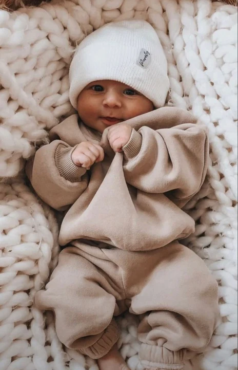Baby in a light brown outfit and white knit hat