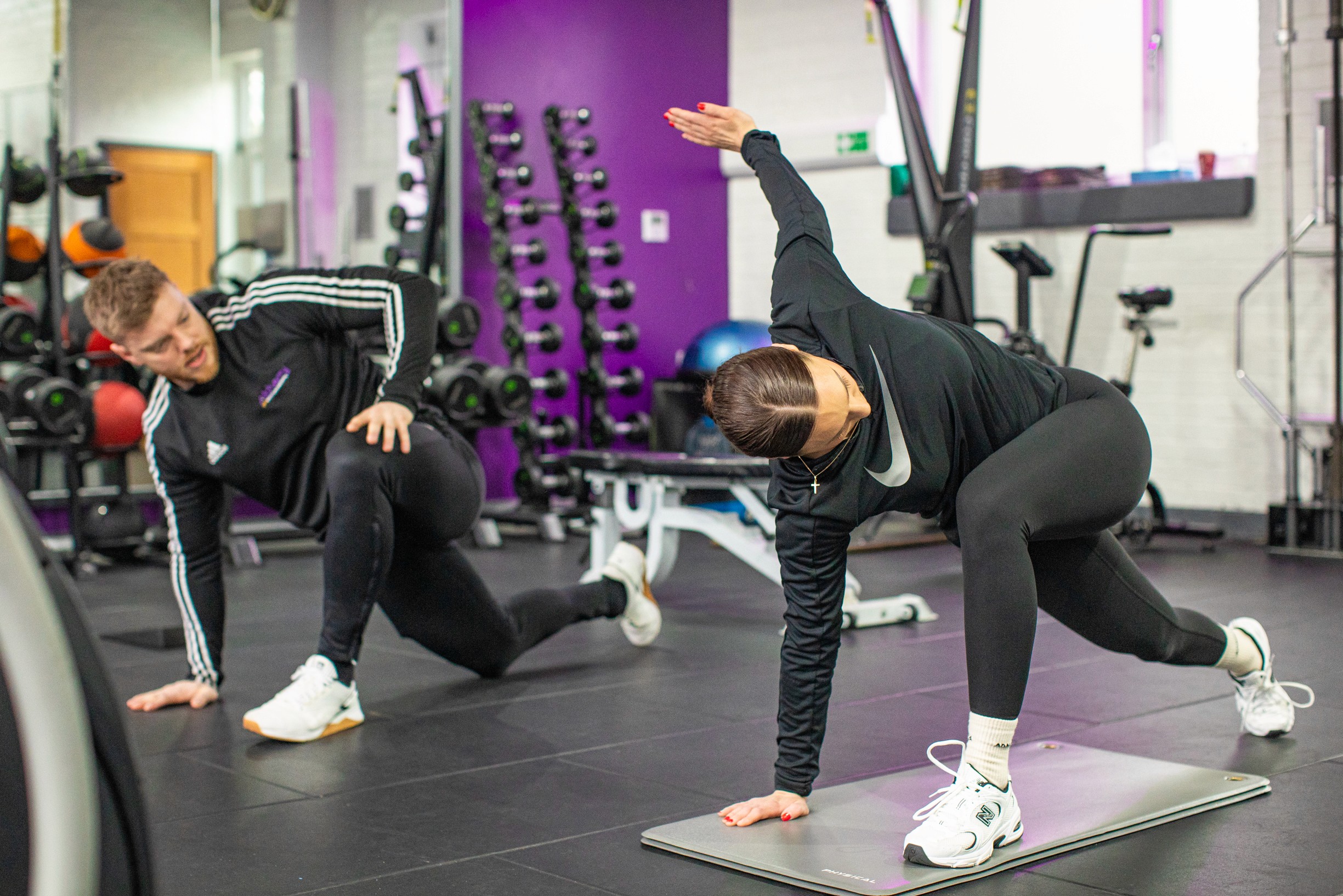 Woman in gym wear doing a mobility exercise as guided by her personal trainer.