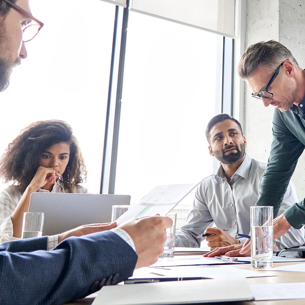 Foto von Mitarbeitern, die gemeinsam an einem Schreibtisch mit Papierkram und Laptops auf dem Tisch arbeiten