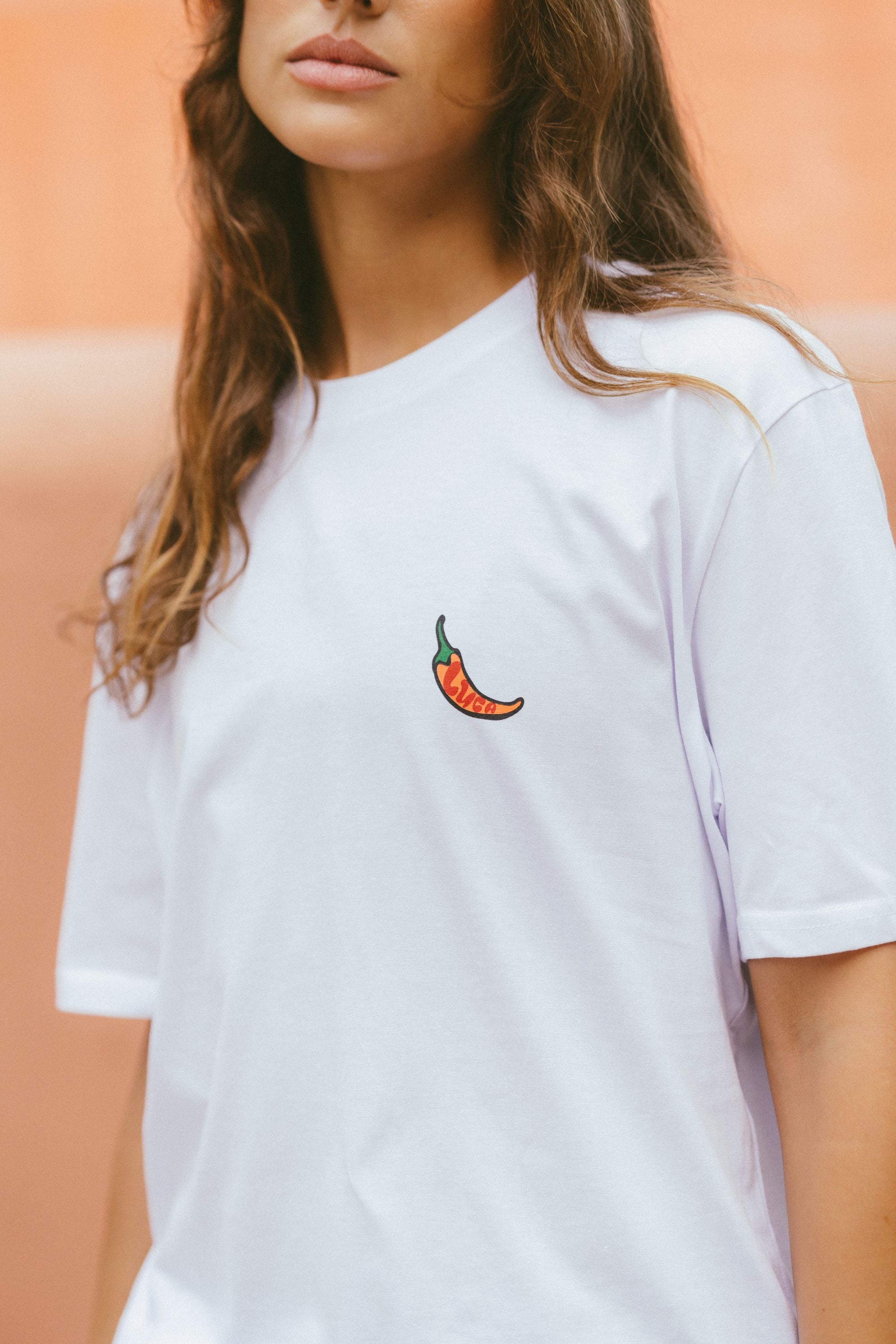 White-t-shirt-with-a-detailed-chili- pepper-embroidery-on-the-chest- modeled-against-a-warm-plain- background