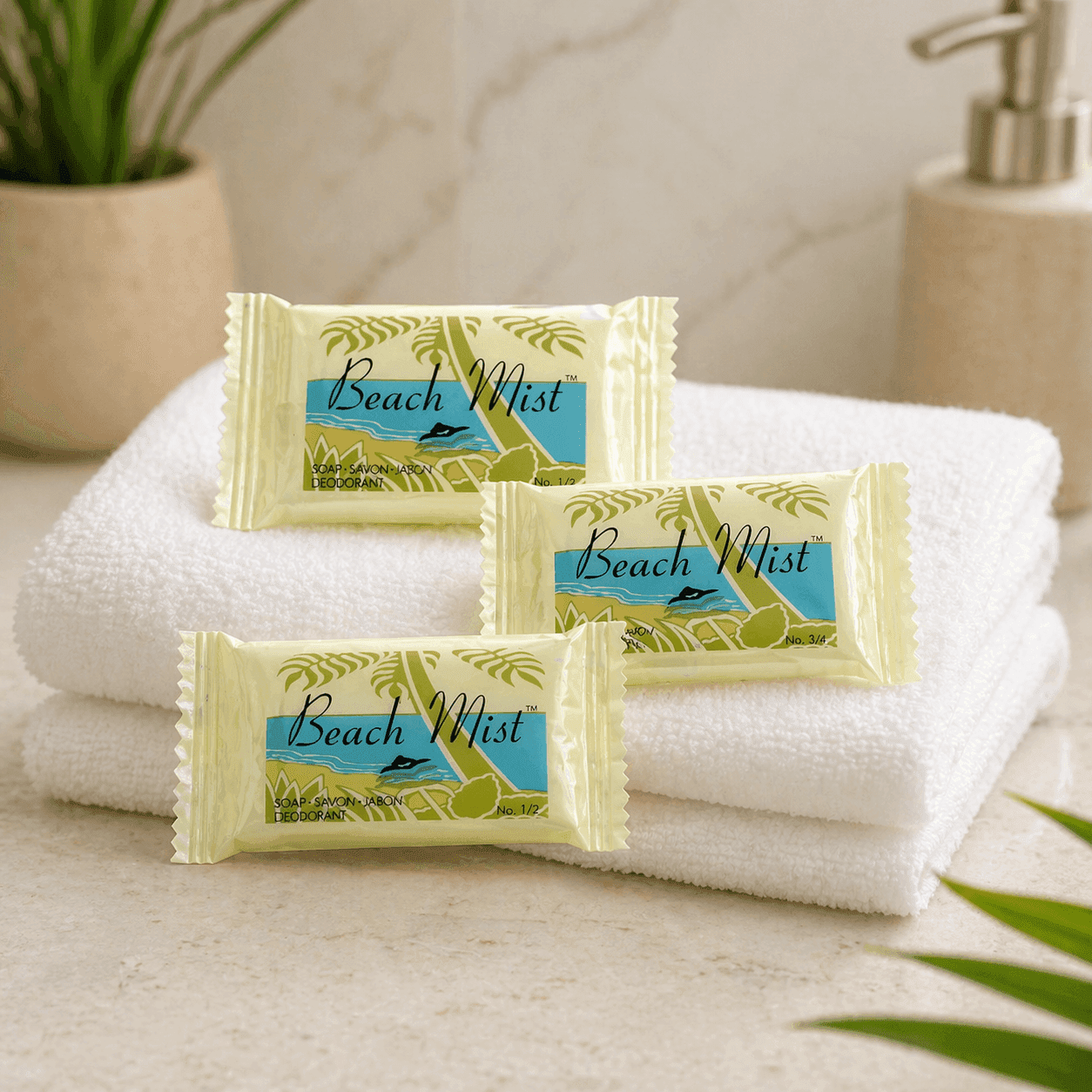 Three individually wrapped Beach Mist soap bars arranged on a folded white towel over a light marble bathroom countertop, with soft natural lighting and a clean hotel-style setting.