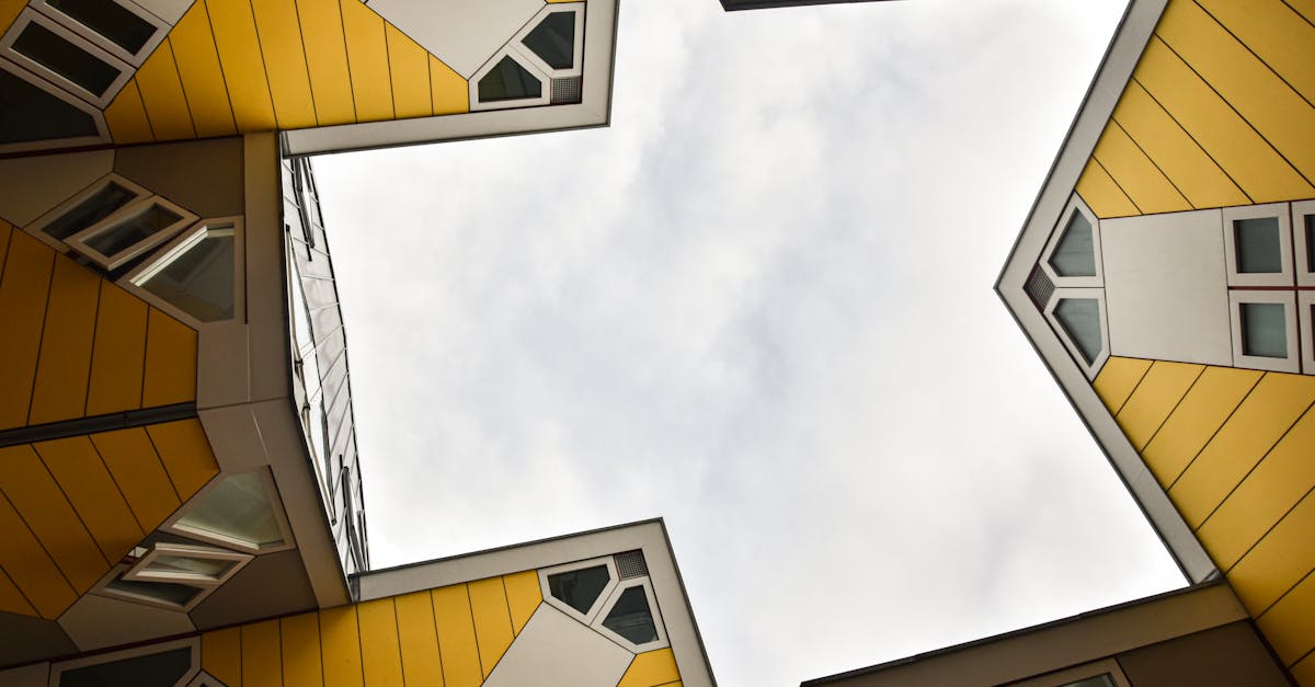 Upward view of yellow cube buildings with geometric design against a cloudy sky.