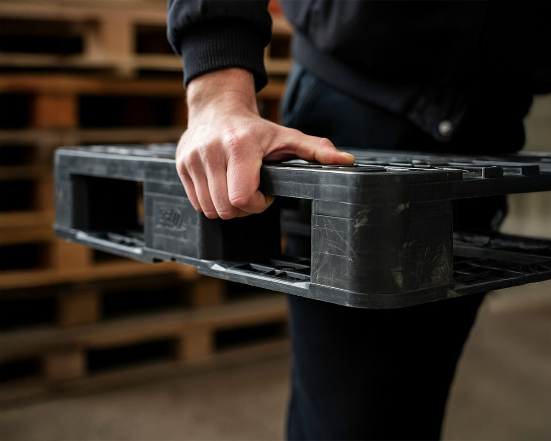 Man holding a black plastic pallet wearing a dark sweater and dark jeans.