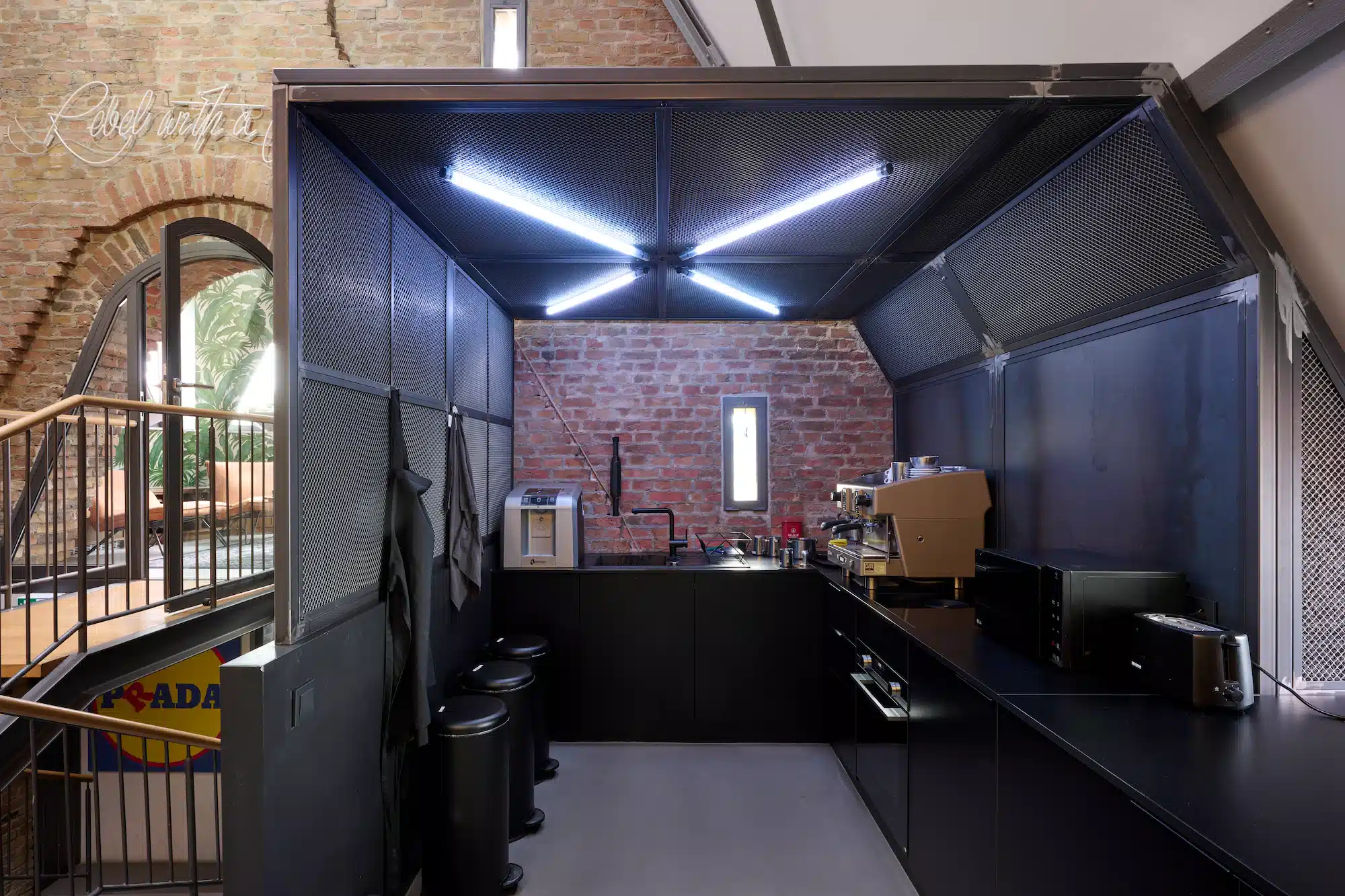 Dojo Office – office kitchen with black fitted furniture, exposed brick wall and neon light ceiling
