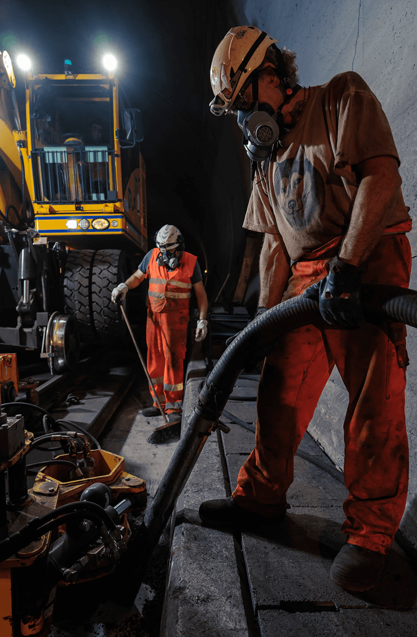 Operatore con maschera respiratoria e DPI che gestisce attrezzature in galleria ferroviaria durante lavori notturni