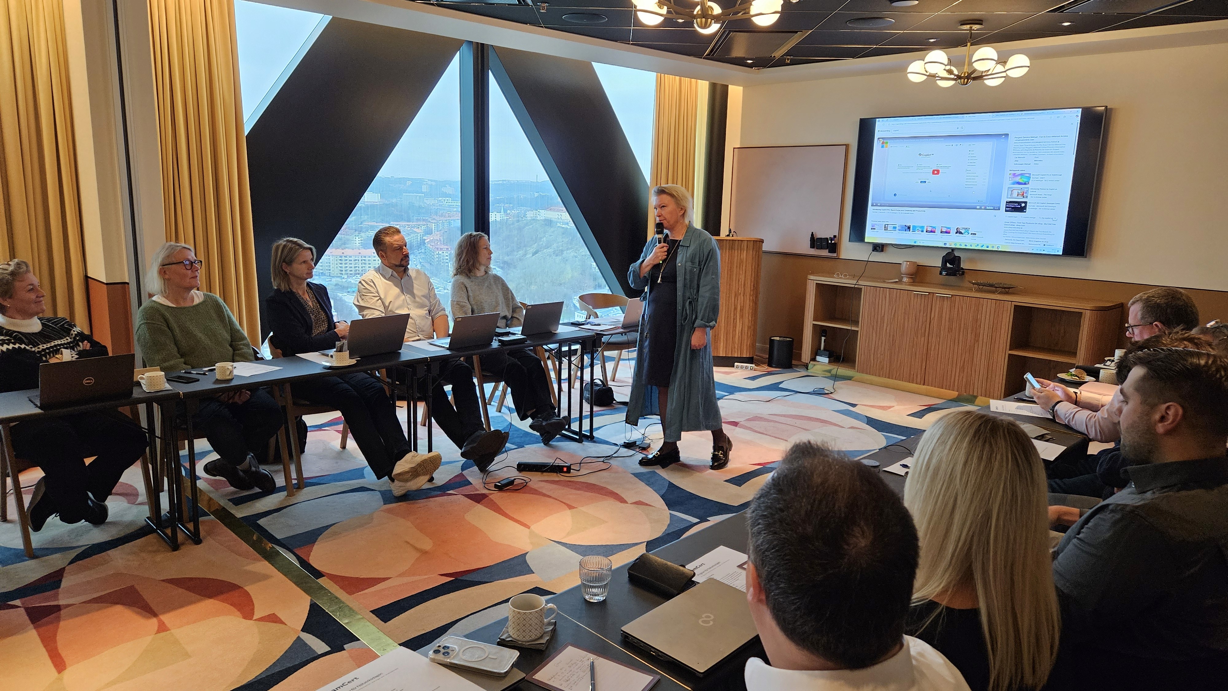 A young person with curly hair smiles at the camera while sitting in front of a laptop against a dark background.