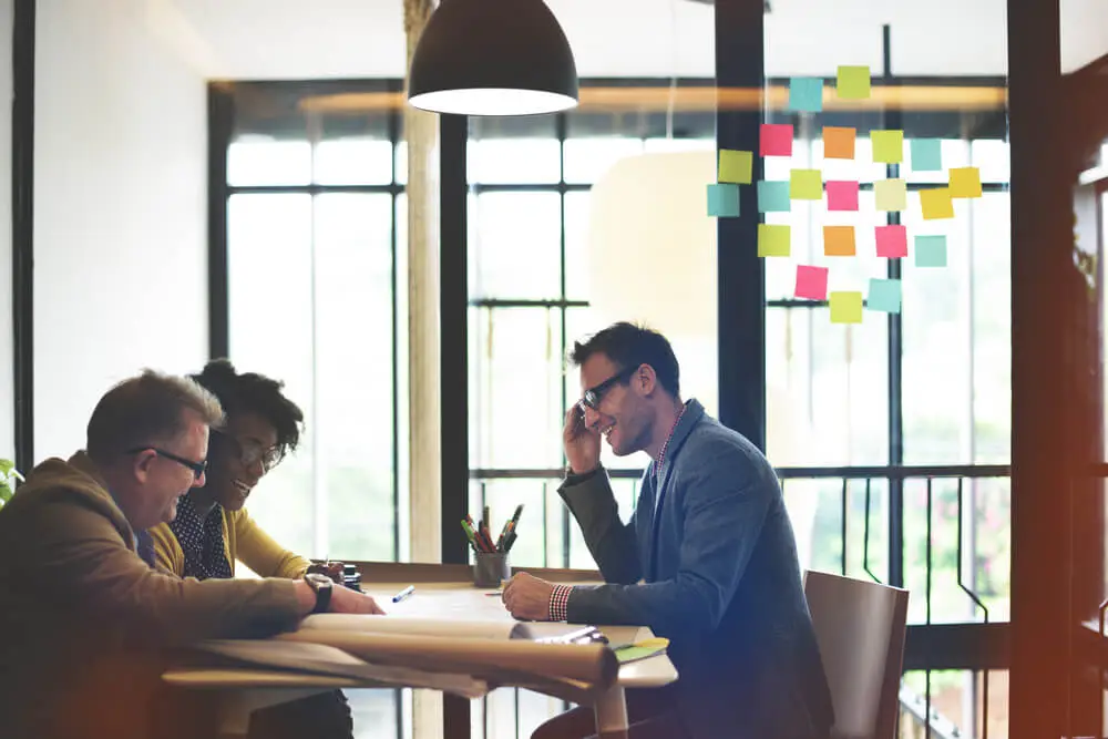 Group of colleagues sitting at a table brainstorming with sticky notes on a glass wall
