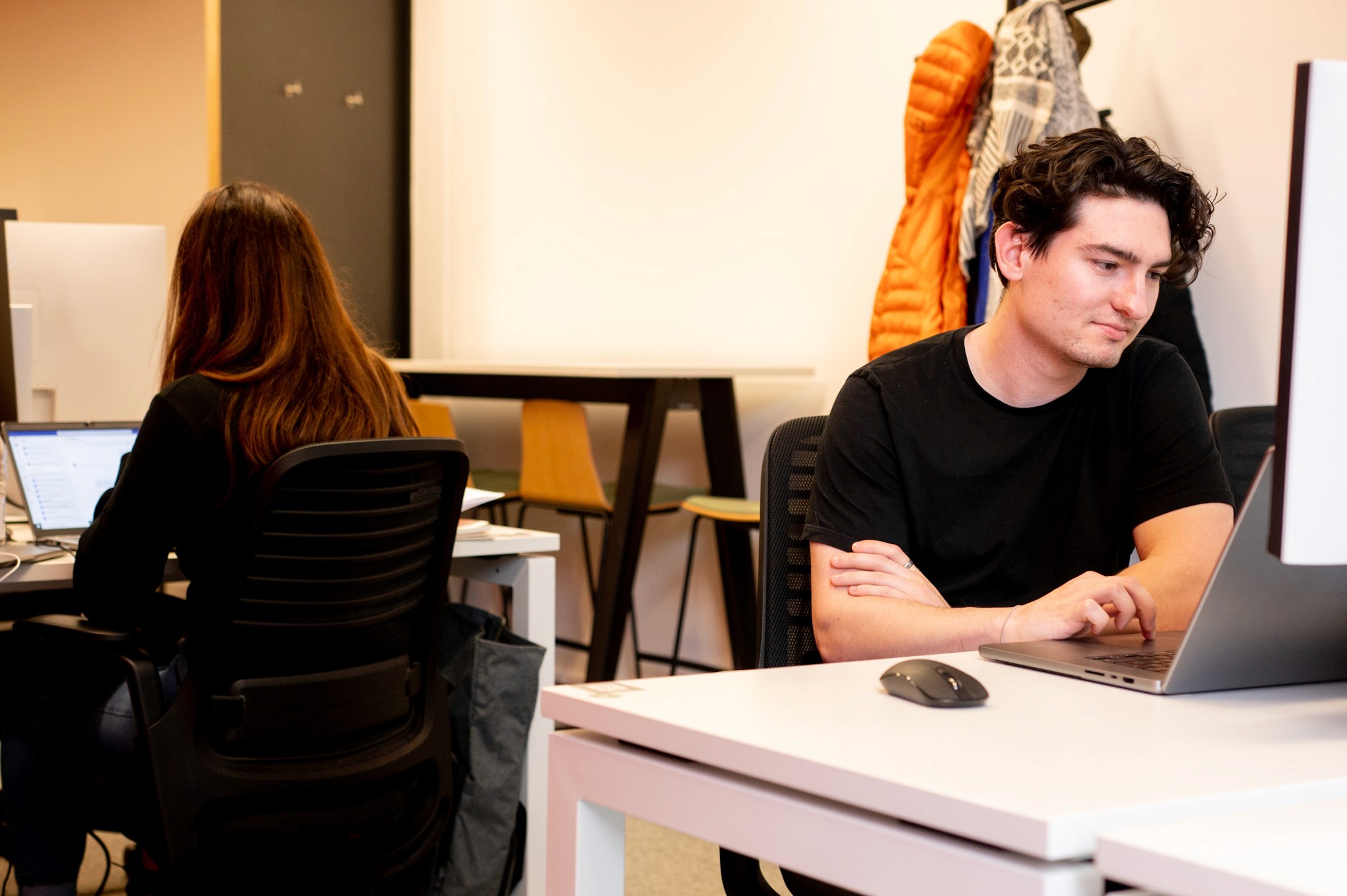 Two people working at desks in a modern office space. One man typing on a laptop, and one woman working at her laptop.