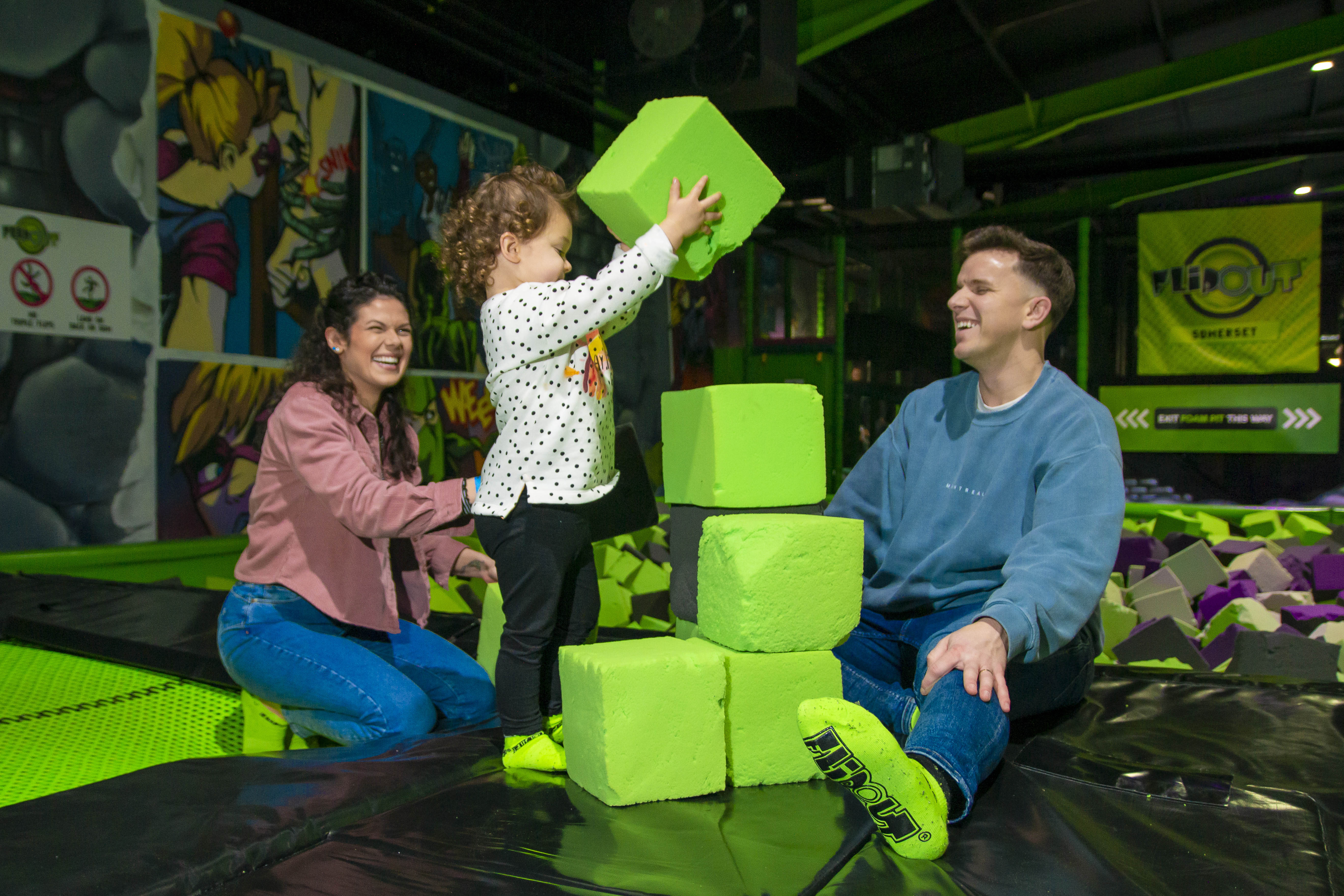 Happy family playing with soft blocks at a bright, colorful indoor play area.