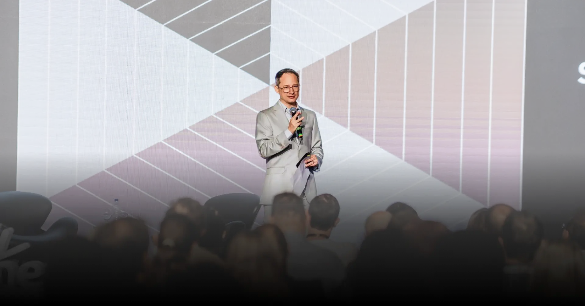 Bg. Foto do dr. Luiz Carlos, psiquiatra, palestrando. Atrás dele está um telão com uma apresentação.