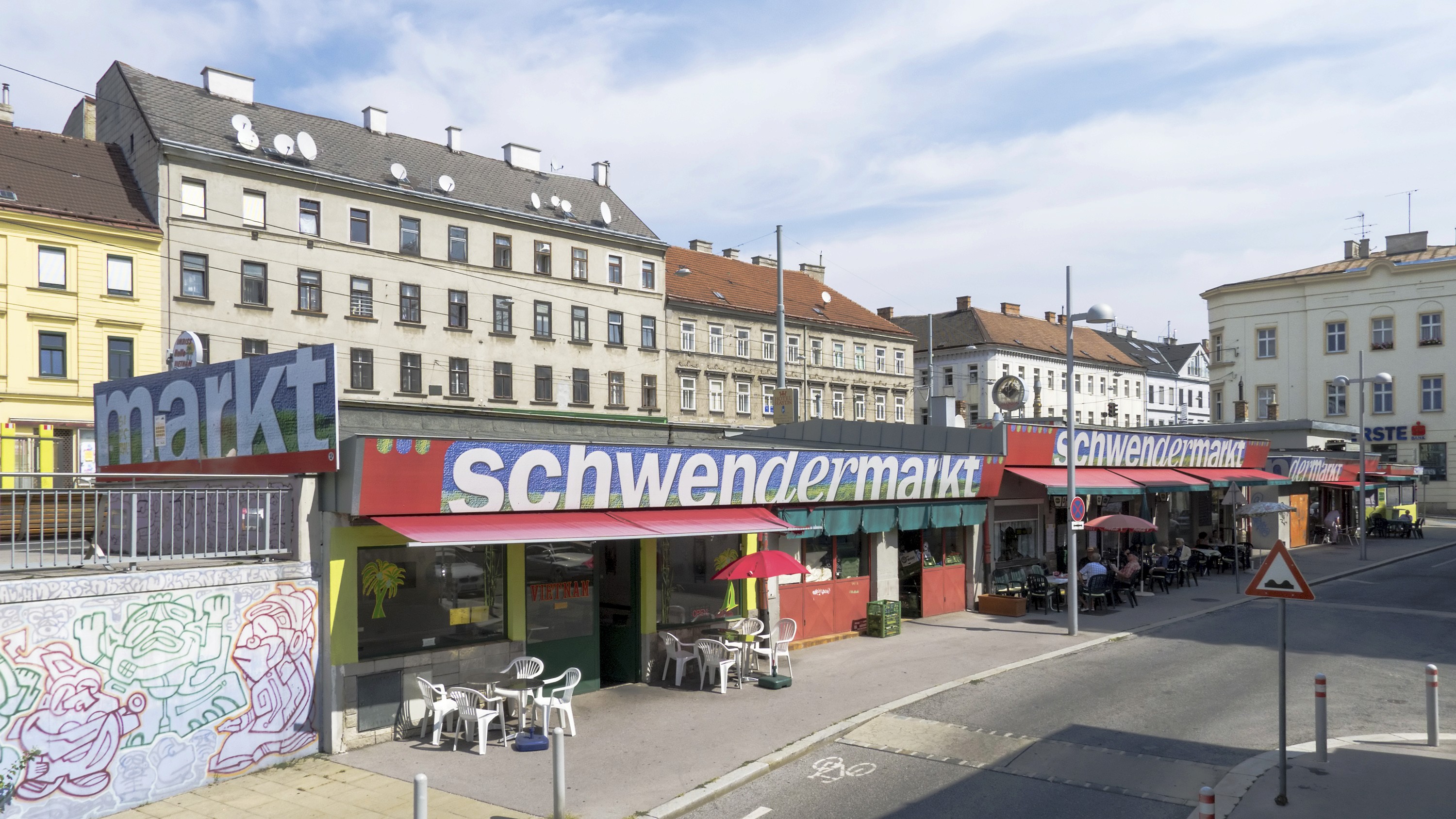 Eine Straßenansicht des Schwendermarkts, mit Gebäuden im Hintergrund unter einem klaren Himmel.