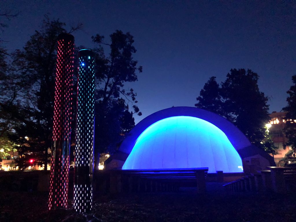Illuminated blue bandshell and colorful light columns at dusk