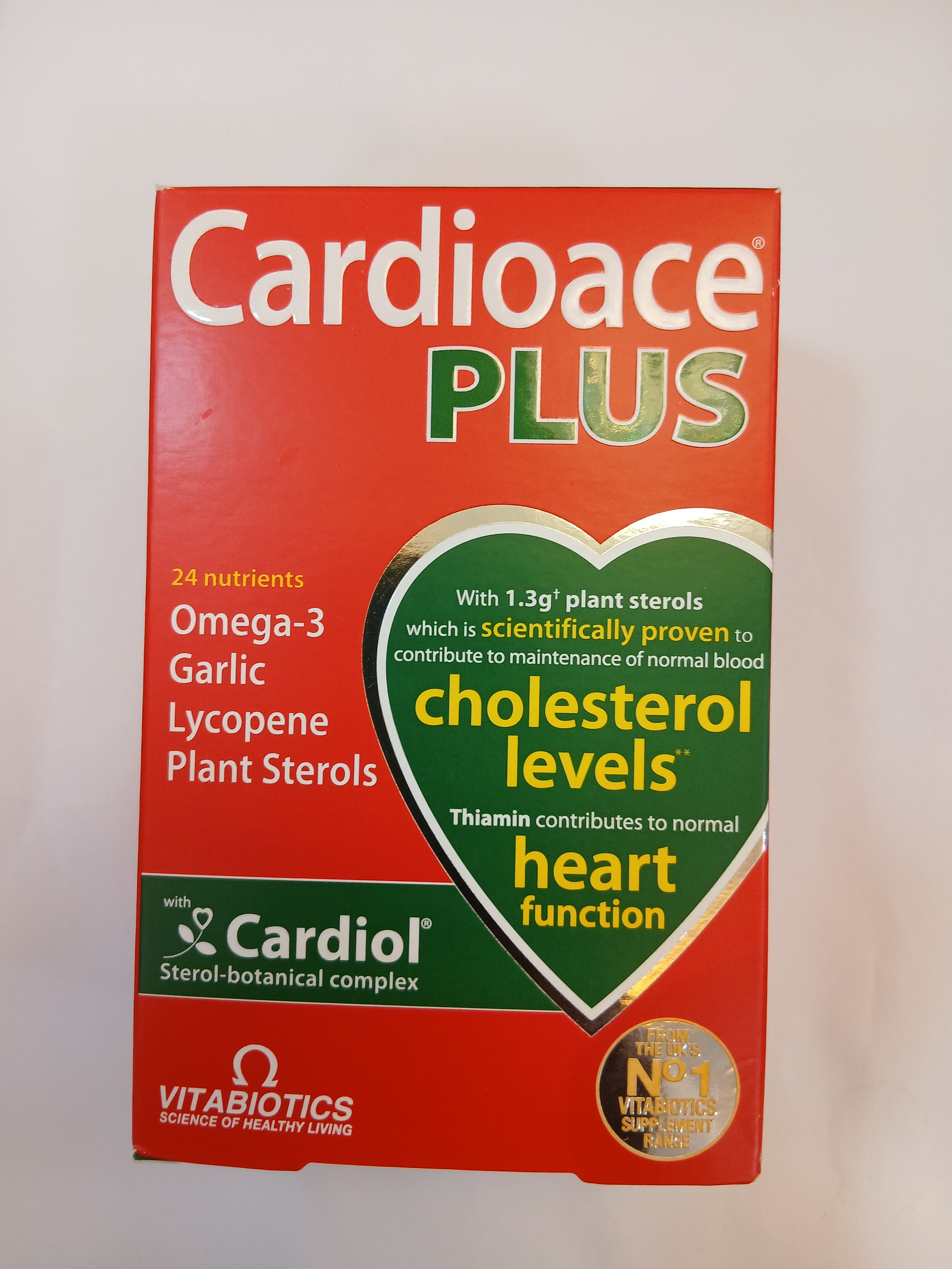 A red and green cardboard box packaging displays nutritional information about a supplement containing 24 nutrients, including omega-3, garlic, lycopene, and plant sterols, with a small circular sticker labeled "Nutri-Score A.