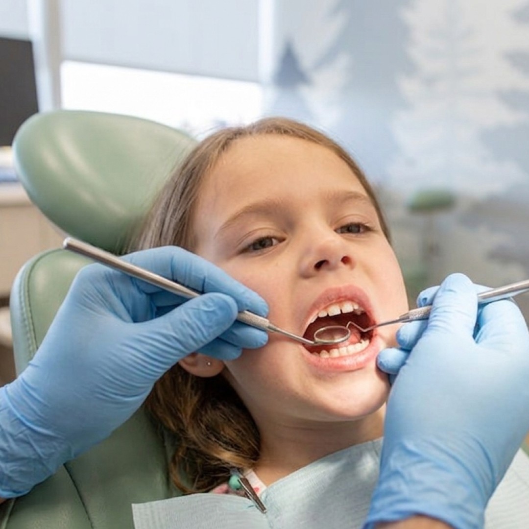 A young girl laying back in a dental chair while Dr. Jeremy performs a gentle tooth examination using dental tools.